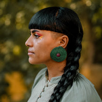 Woman with braided hair and green earrings against a blurred natural background