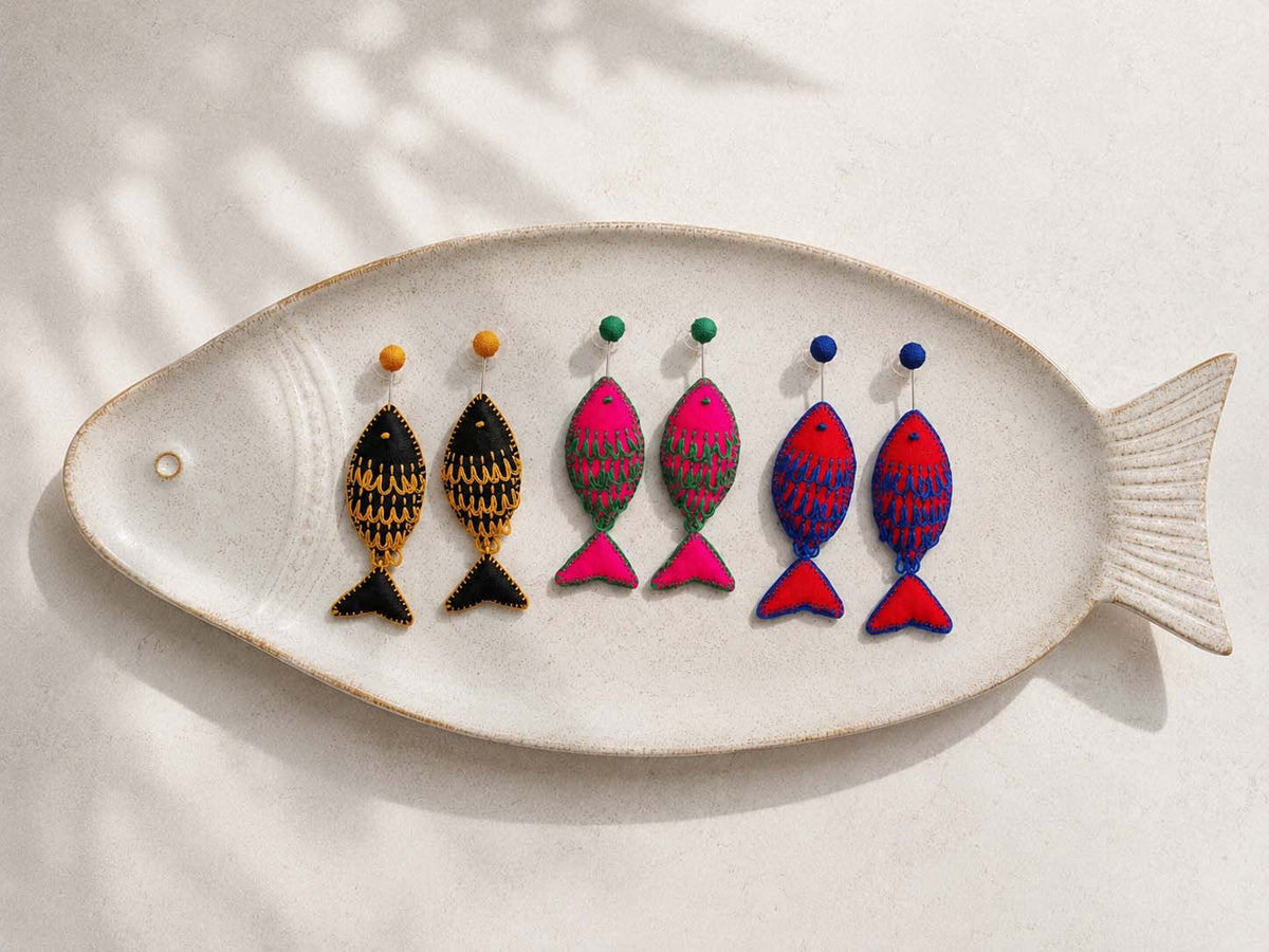 Three color variations of Rui handmade fish-inspired textile stud earrings, namely black, pink and red, displayed on a fish shaped ceramic platter.
