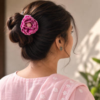 A woman shown from the back wearing a pink fabric Phoolwanti Bun pin  hair accessory with a small central floral detail, styled in a bun. She is wearing a light pink embroidered top against a softly blurred background.