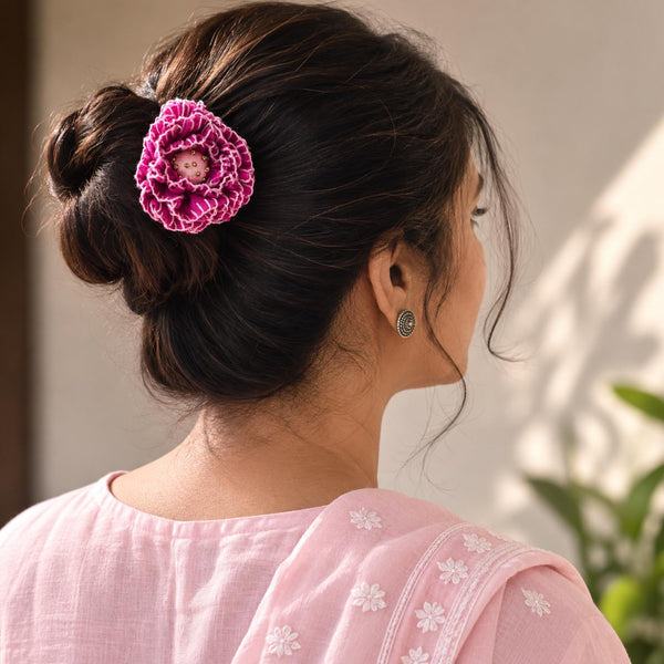 A woman shown from the back wearing a pink fabric Phoolwanti Bun pin  hair accessory with a small central floral detail, styled in a bun. She is wearing a light pink embroidered top against a softly blurred background.