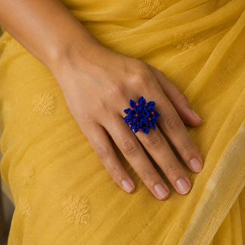 A close-up of a hand wearing a handcrafted blue shiuli ring, resting on a yellow embroidered fabric.