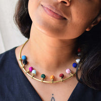 A close-up of a person wearing a brass metal necklace with multiple small colorful, movable handmade fabric beads in blue, pink, green, orange, red, and white.