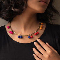Al cose-up of a woman wearing a brass Kalpana necklace with small hanging movable fabric beads in pink, blue, red, and yellow, paired with a black top.