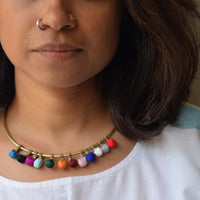 A close-up of a person wearing a  brass toned necklace with multiple small colorful fabric movable beads  in colors of pink, blue, orange, green, red, and white.