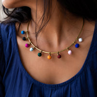 A close-up of a woman wearing a handcrafted Kalpana necklace with small fabric colorful beads hanging along a curved brass metal wire neckpiece.