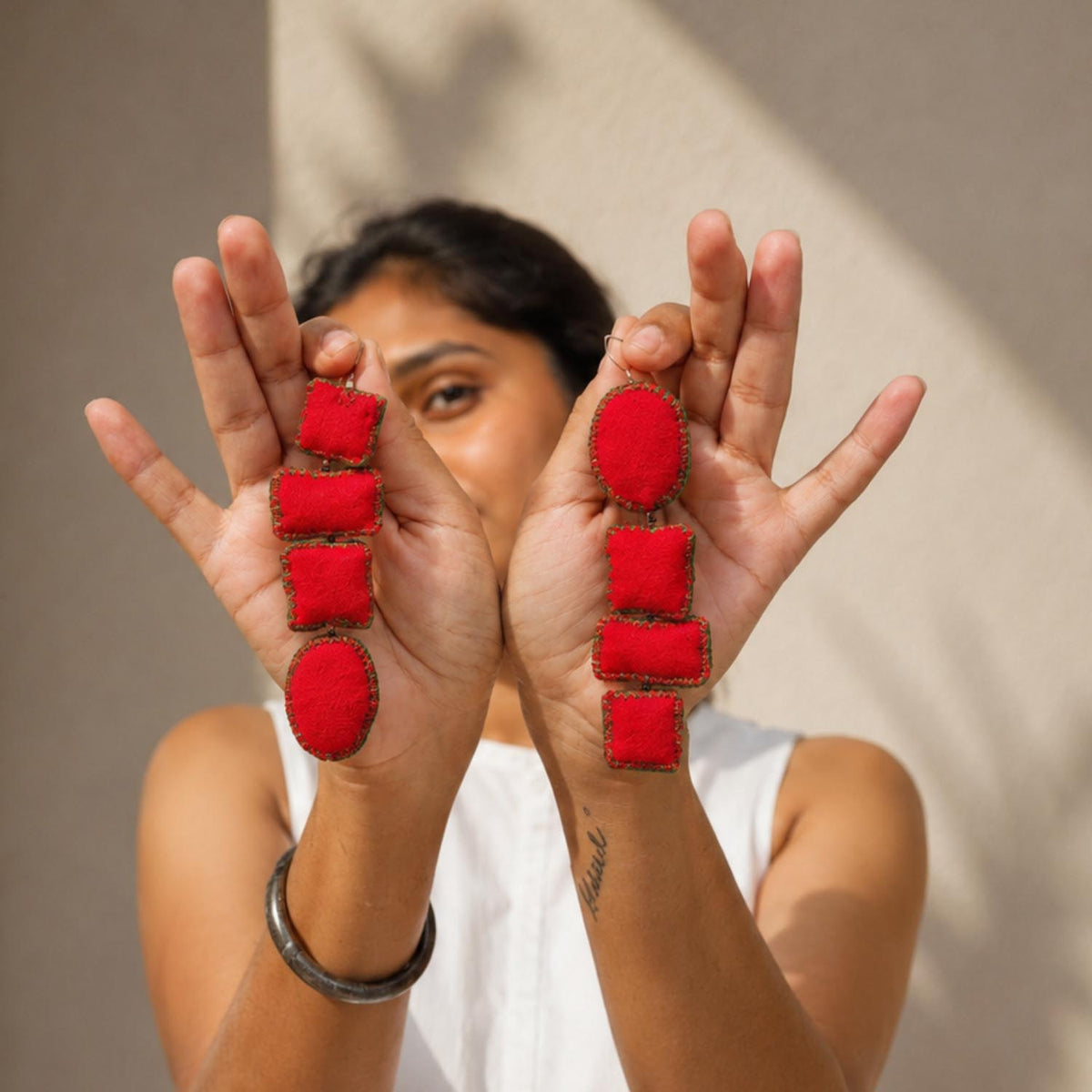 A person holds up their hands to show a pair of asymmetric red Nirali fabric earrings.