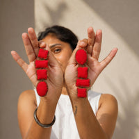A person holds up their hands to show a pair of asymmetric red Nirali fabric earrings.