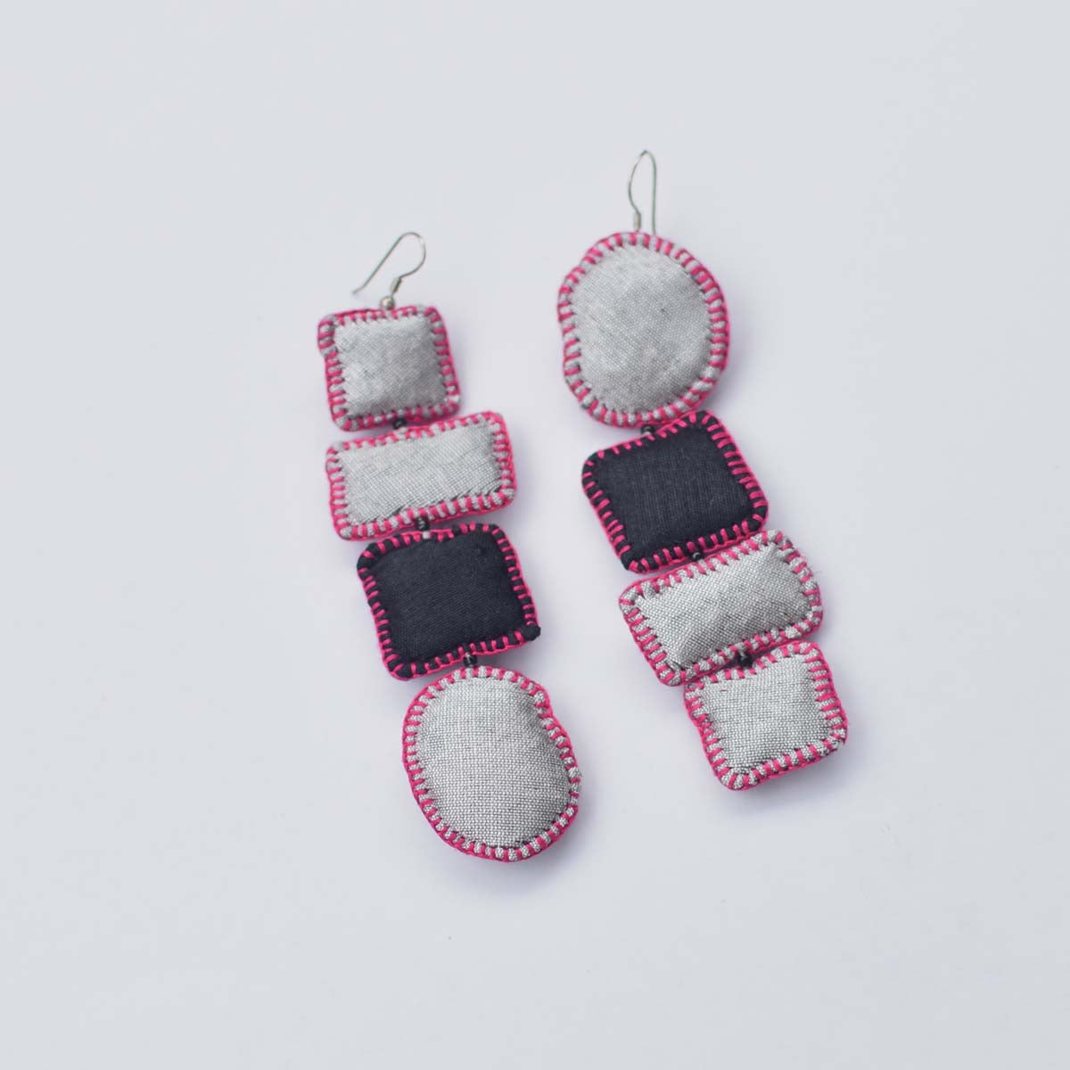 A pair of handmade dangle earrings made from fabric pieces in silver, black, and pink, displayed on a clean white background.