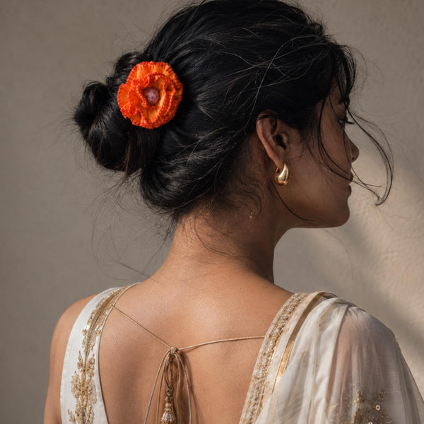A woman shown from the back and side wearing a bright yellow fabric Phoolwanti flower hair accessory tucked into her dark hair, paired with a cream and gold embroidered top against a neutral beige background.