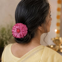 a woman with silver hair wears the handmade Phoolwanti baby pink fabric floral bun pin to secure her hair knot, in a festive dressup.