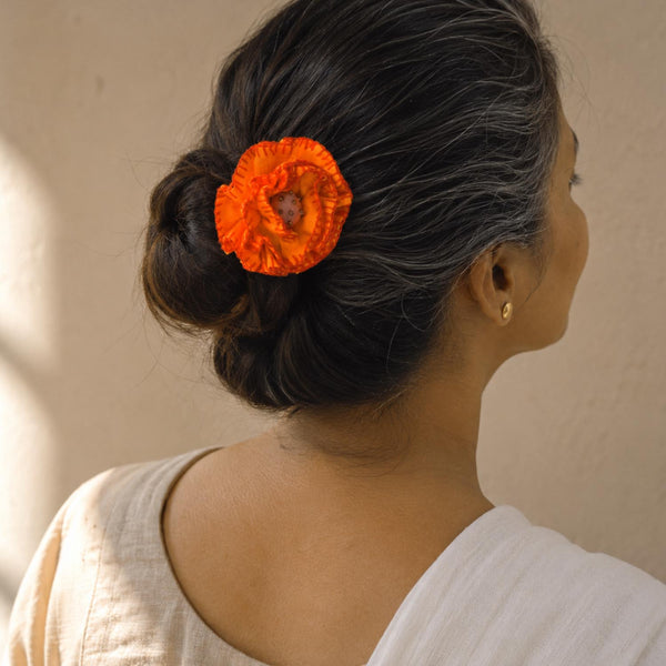 A woman shown from the back and side wearing a bright yellow fabric Phoolwanti flower bun pin  hair accessory in her dark hair, against a warm beige wall.