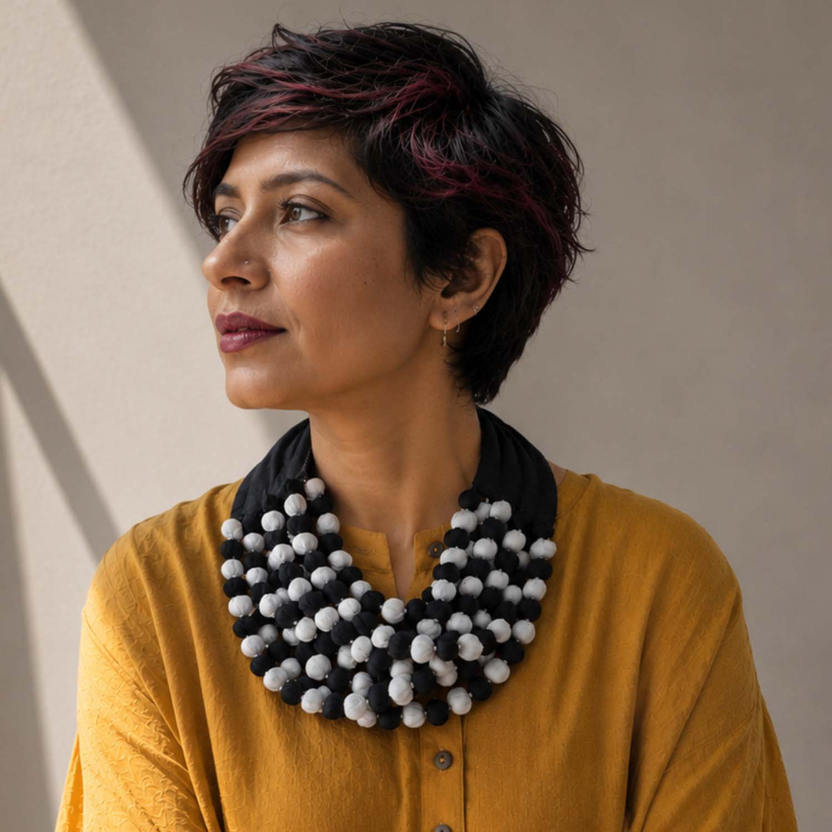 model with short dark hair wearing a handcrafted Ratna textile pompom collar necklace in black and white combo.