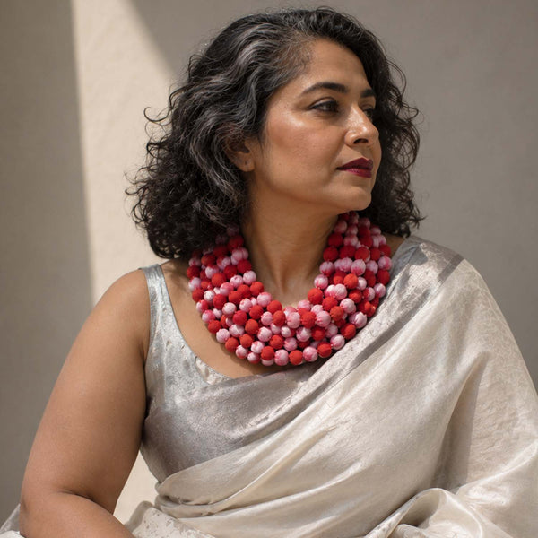 A woman with dark curly hair wearing a Ratna chunky beaded necklace in red and pink, paired with a light silver satin sari. 