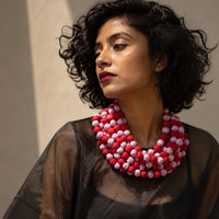 model wearing Ratna multi-strand beaded necklace made of alternating red and light pink fabric beads, paired with a sheer black top.