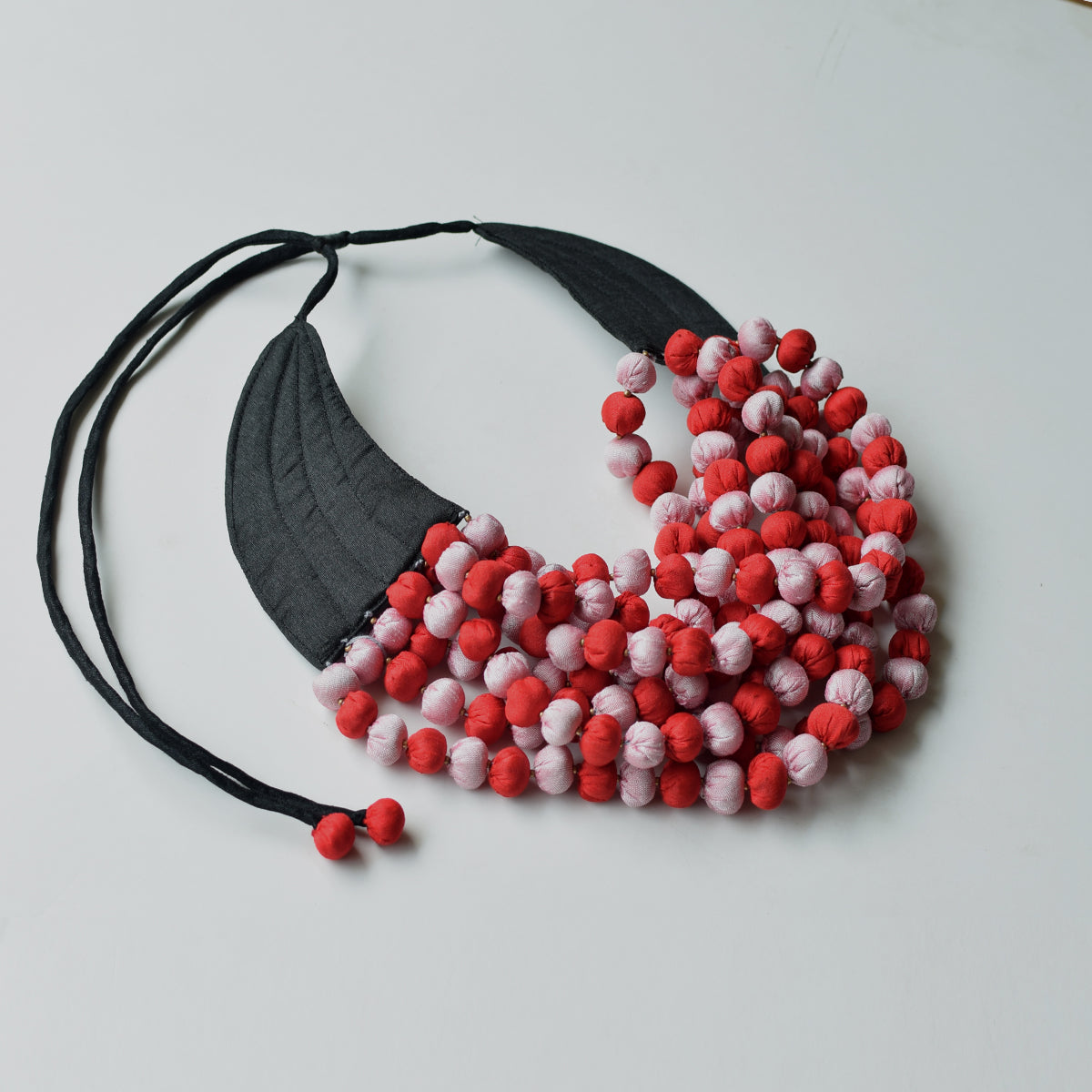 Flatlay photo of Ratna black collar neckpiece in red and pink handmade fabric beads.