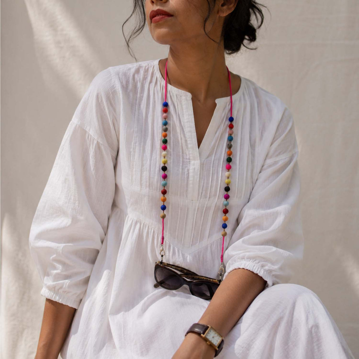 A woman wearing a white dress, accessorized with a vibrant, multicolored beaded Sanchita specs retainer string with the sunglass hanging to it.