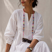 A woman wearing a white dress, accessorized with a vibrant, multicolored beaded Sanchita specs retainer string with the sunglass hanging to it.