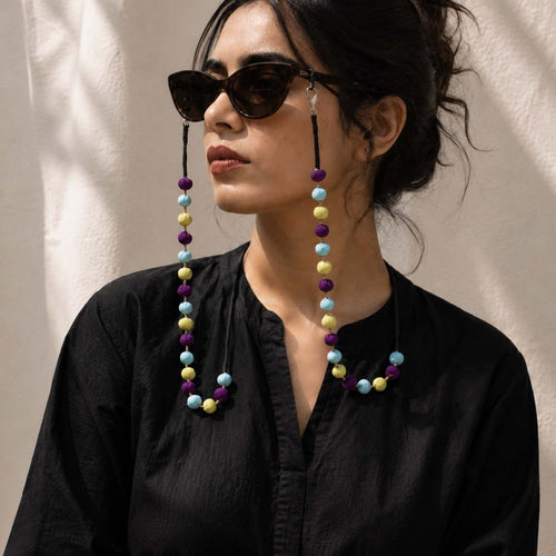 A woman wearing colorful Sanchita eyeglass chain handmade with  baby blue, purple and lemon yellow fabric beads.