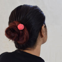 A person's head from the back, wearing a red Sarala handcrafted fabric bead bun stick hair accessory with a white running hand-embroidery.