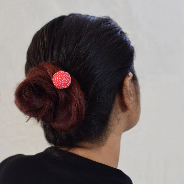 A person's head from the back, wearing a red Sarala handcrafted fabric bead bun stick hair accessory with a white running hand-embroidery.