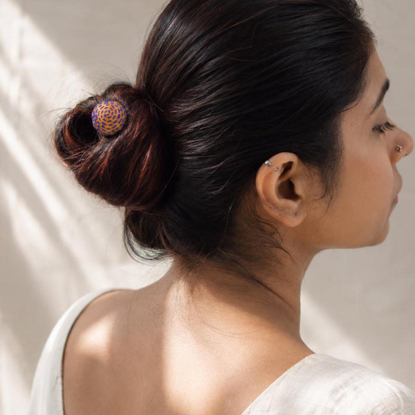 A woman shown from the back and side profile wearing a dark hair bun secured with Sarala bun stick in Yellow fabric and handembroidered in blue running stitch.