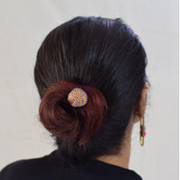 A person's head from the back, wearing a simple Sarala bun stick hair accessory, made of brass metal, handcrafted fabric bead and handembroidered with blue thread.
