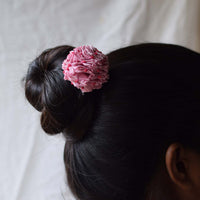 A person's hair styled in a bun with a handcrafted baby pink Shiuli bun stick, hair accessory on top.