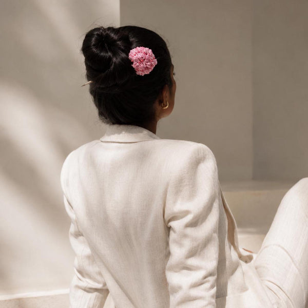 A woman seen from behind wearing a handmade Shiuli pink flower hair accessory in her dark hair, dressed in a white linen jacket and pants.