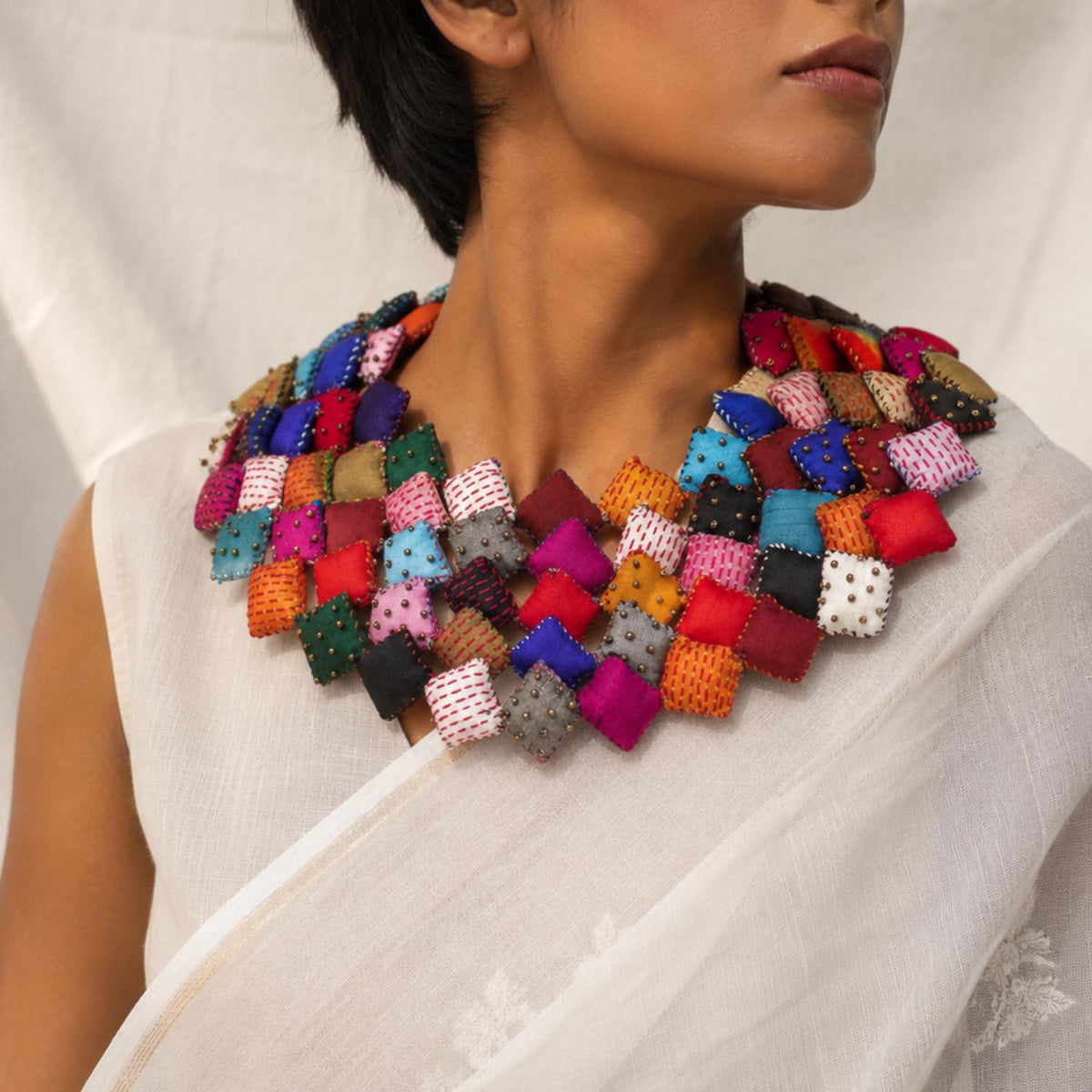 close-up shot of a model wearing a Tejaswini fabric bib necklace made of many colorful square fabric pieces, paired with a white saree.