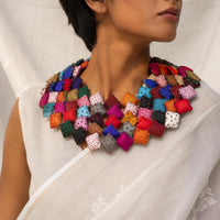 close-up shot of a model wearing a Tejaswini fabric bib necklace made of many colorful square fabric pieces, paired with a white saree.