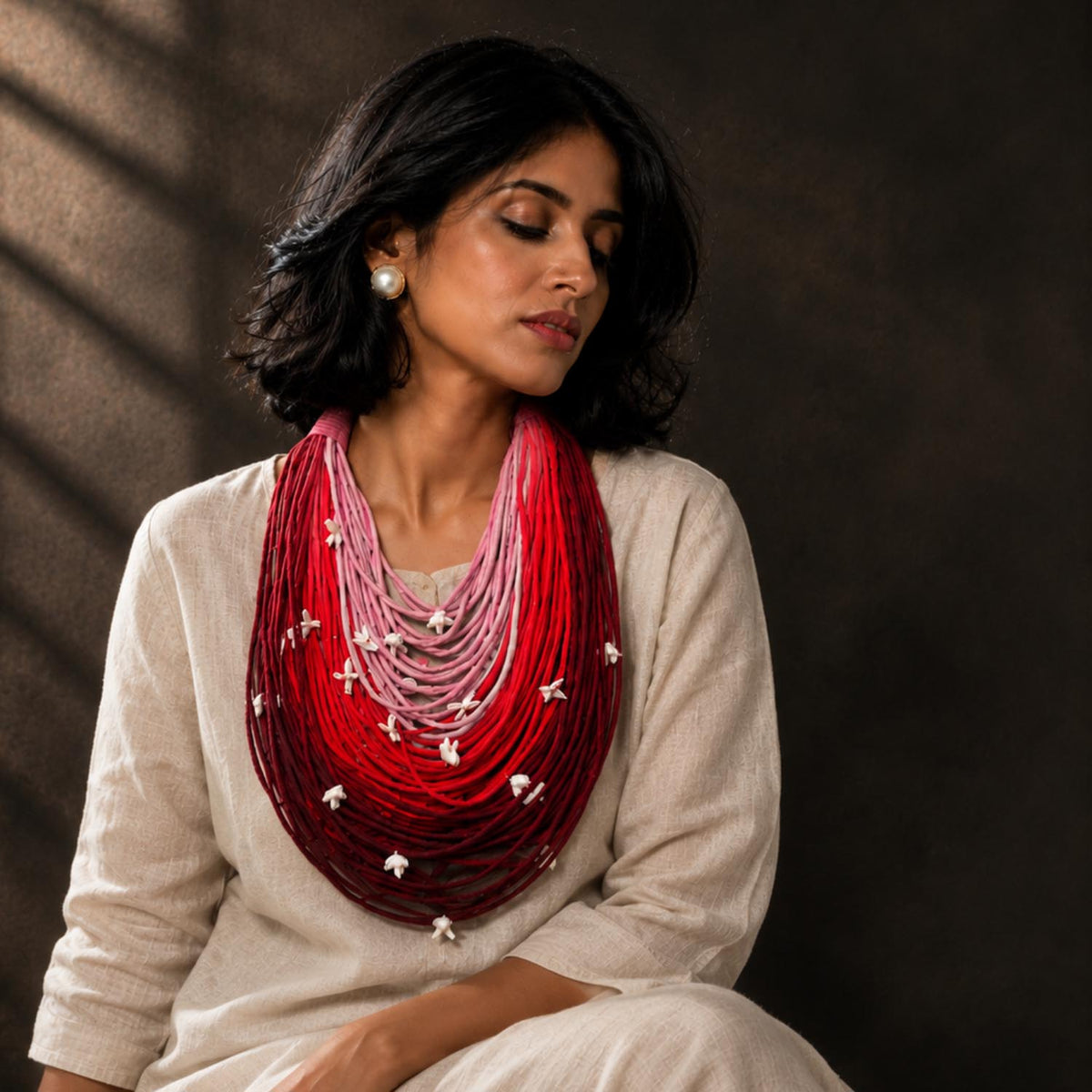 A woman wearing a cream-colored linen outfit and grand statement Vanya necklace in shades of red, pink, and maroon with adjustable tiny florals