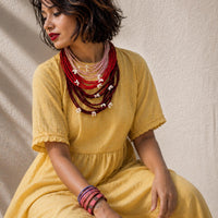 A woman wearing a mustard yellow dress and layered red, pink, and maroon Vanya neckpiece.