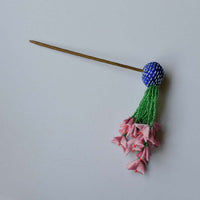 Flat lay of Zubeida bun stick hair accessory with blue fabric ball, green beaded strings that end in light pink tiny handcrafted fabric flowers
