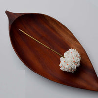 Shiuli textile floral Bun stick hair accessory shot up close over a wood base tray in leaf shape, to show details.