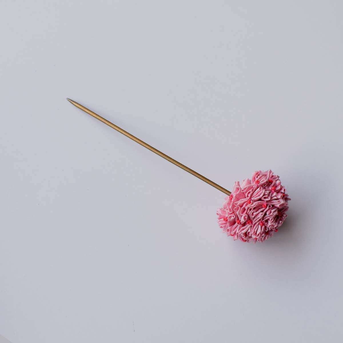 Flat lay of the handmade Shiuli metal bun stick hair accessory which is made of cluster of many tiny flowers in baby pink.