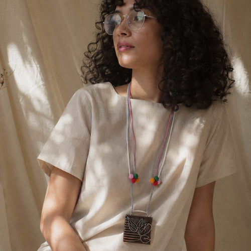A model wearing the length adjustable Kavita textile neckpiece, that carries a hand carved wooden pendant with leaf design.
