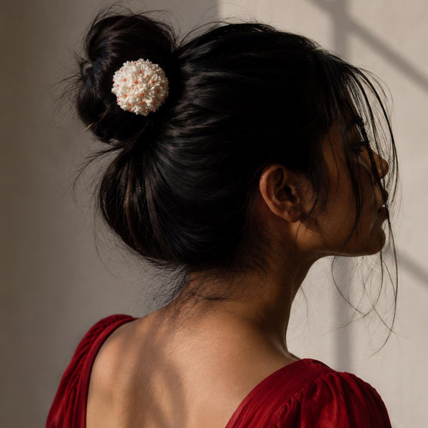 A woman shown from the back and side profile wearing a dark hair bun secured with a Handcrafted shiuli bunstick, against a warm-toned wall with soft window shadows.