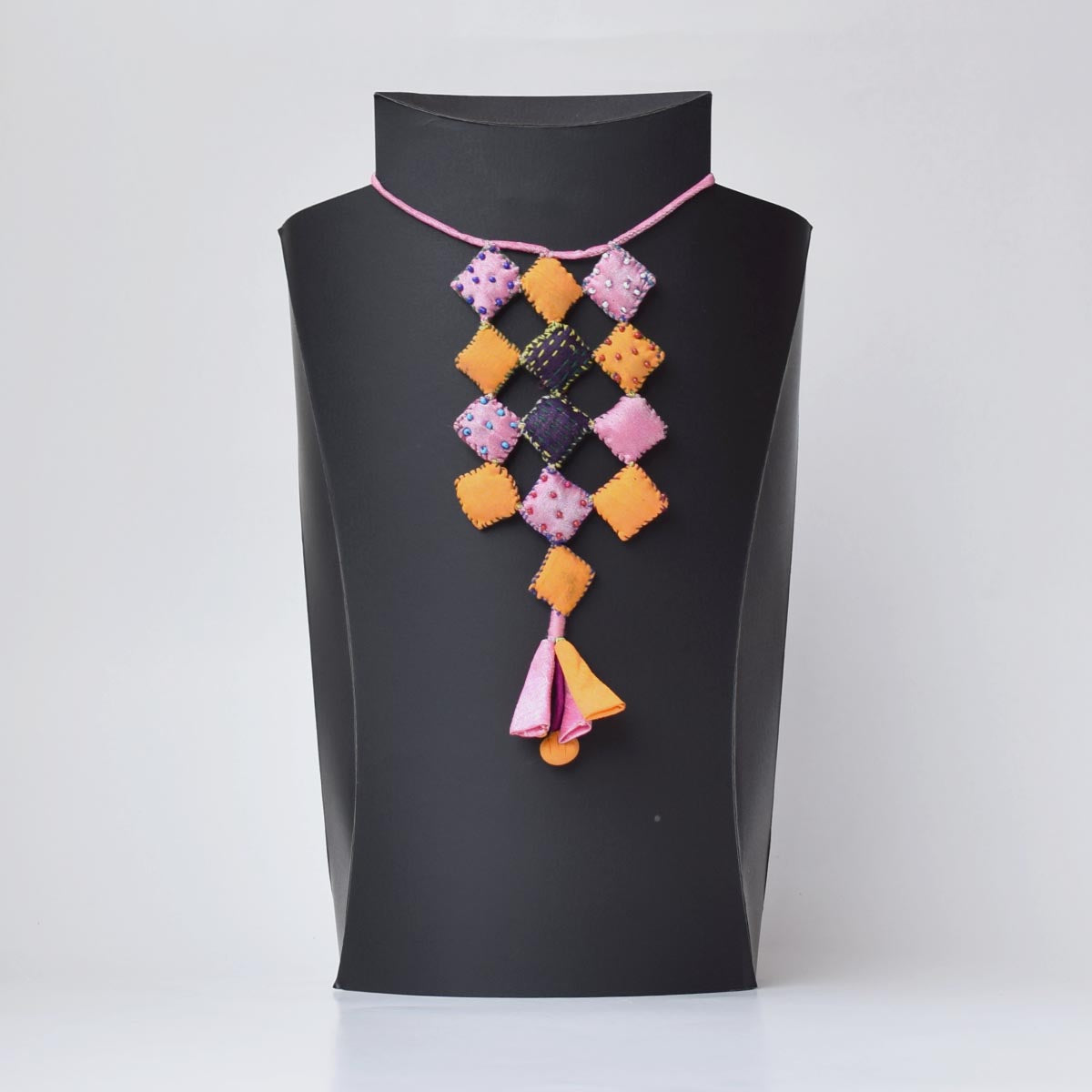 Ayanti handmade fabric neckpiece displayed on a black mannequin, featuring square pillows and a tassel.
