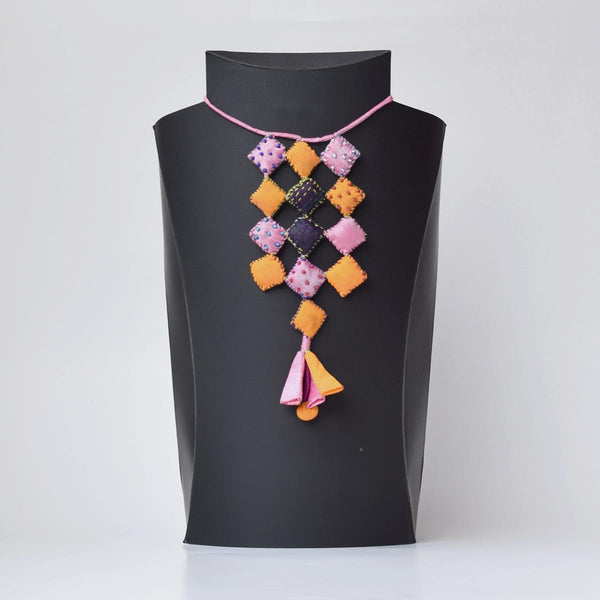 Ayanti handmade fabric neckpiece displayed on a black mannequin, featuring square pillows and a tassel.