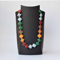 A multicolored square pillow Keya neckpiece with a variety of shapes displayed on a mannequin.