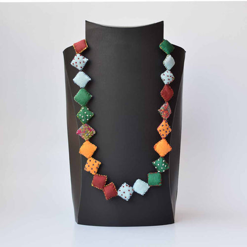 A multicolored square pillow Keya neckpiece with a variety of shapes displayed on a mannequin.