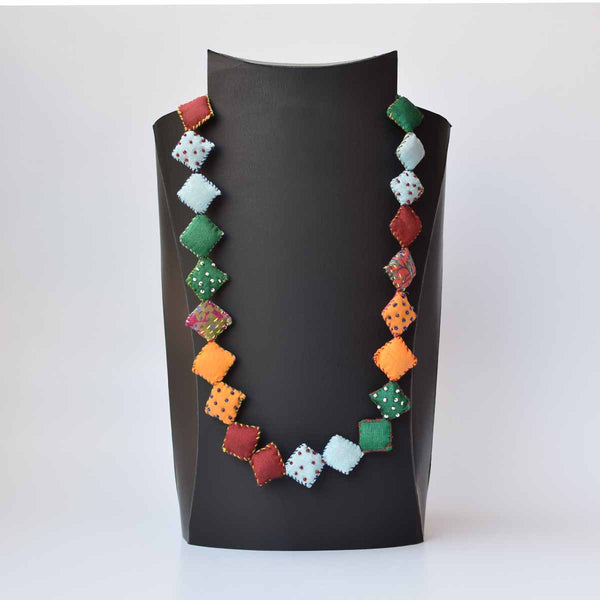 A multicolored square pillow Keya neckpiece with a variety of shapes displayed on a mannequin.
