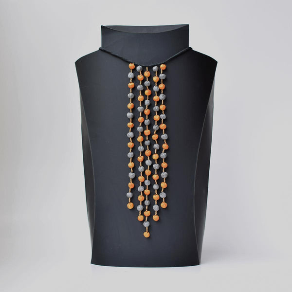 A neckpiece displayed on a mannequin, composed of tiny fabric beads in gray and orange, arranged in multiple strands.