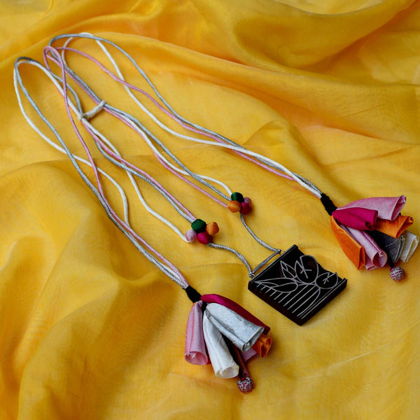 Kavita neckpiece with colorful fabric baubles and a handcrafted wooden block pendant, displayed against a yellow fabric background.